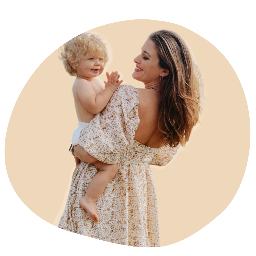 A round photo with a tan background and a woman with light brown here in a flowy floral dress smiling, looking over her shoulder at the curly-headed blonde son she's holding