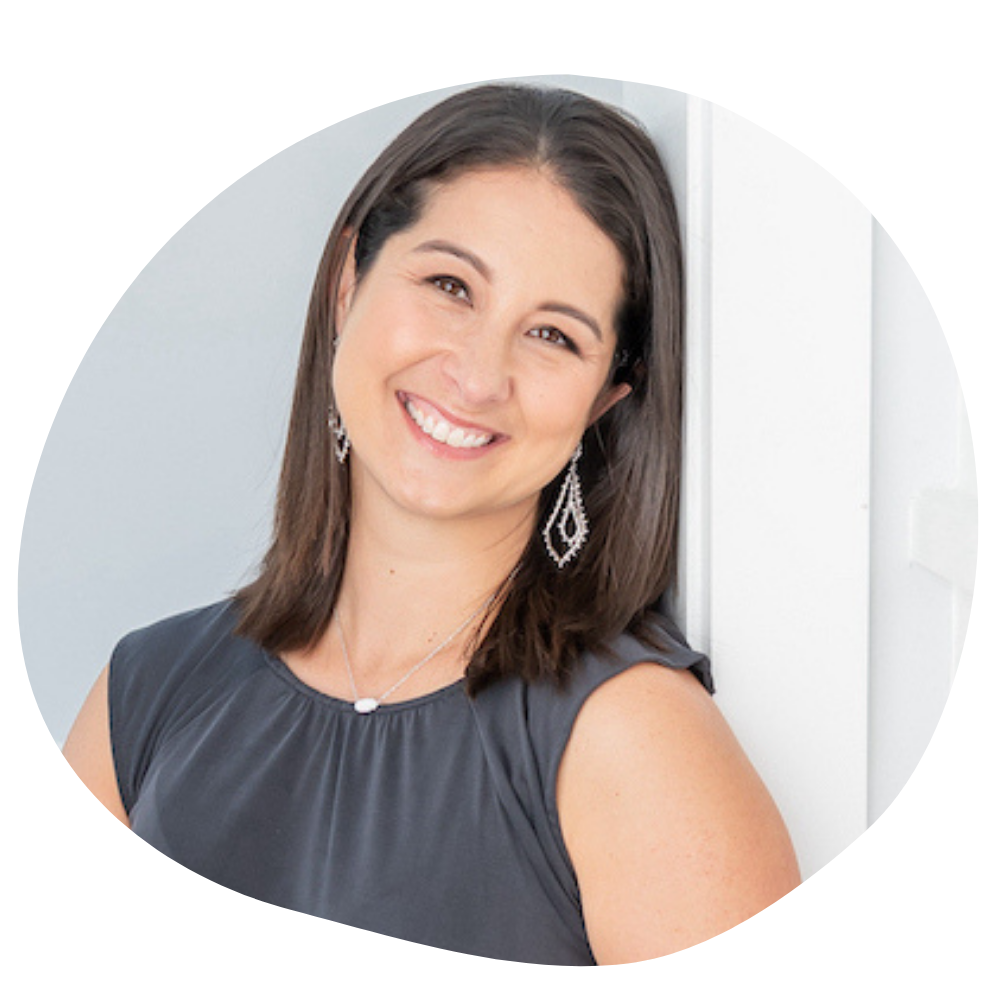 A woman with olive skin and shoulder-length brown hair leans her head against a wall with a soft, gentle smile