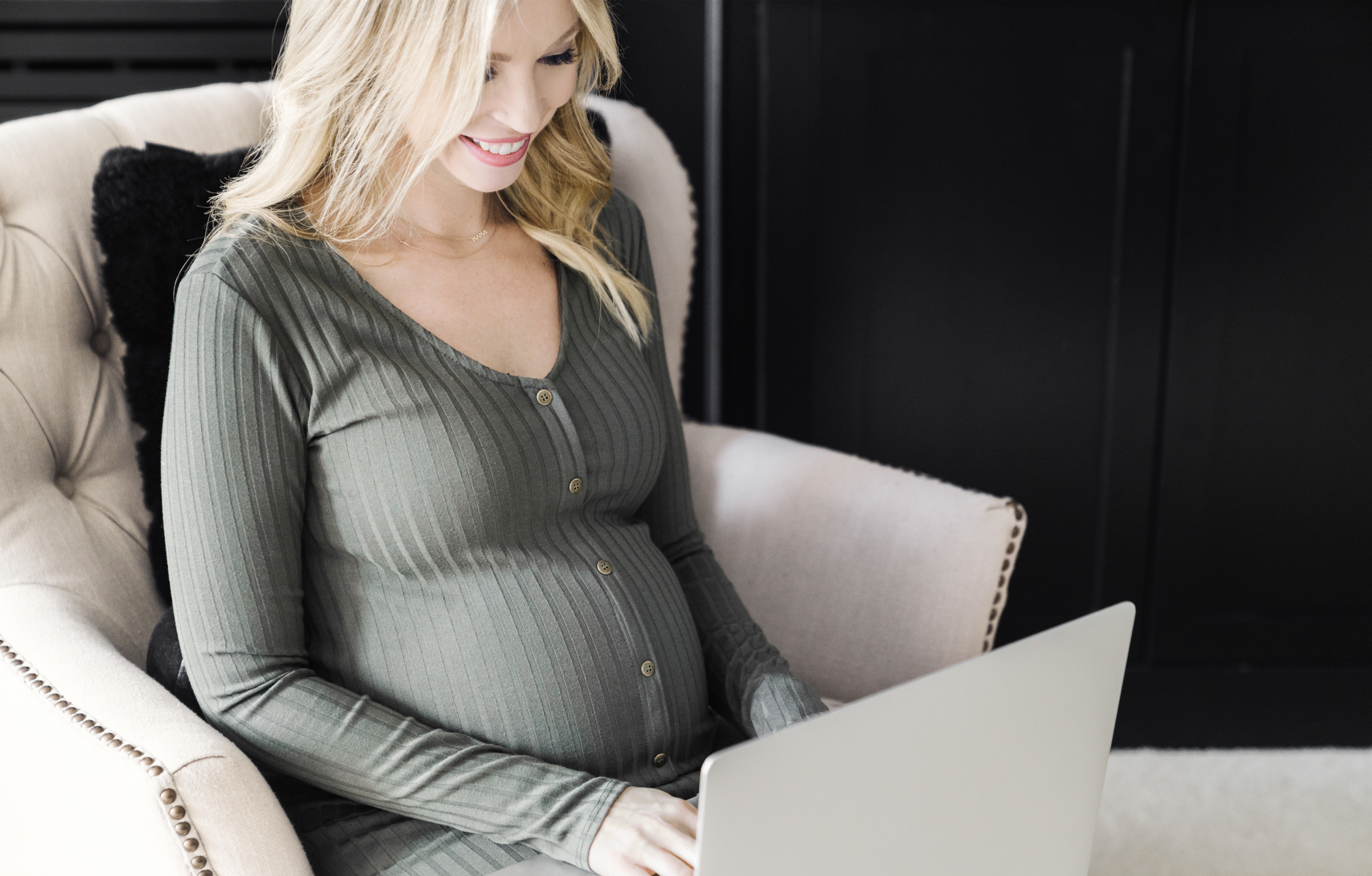 Blonde pregnant woman sits in chair with laptop 