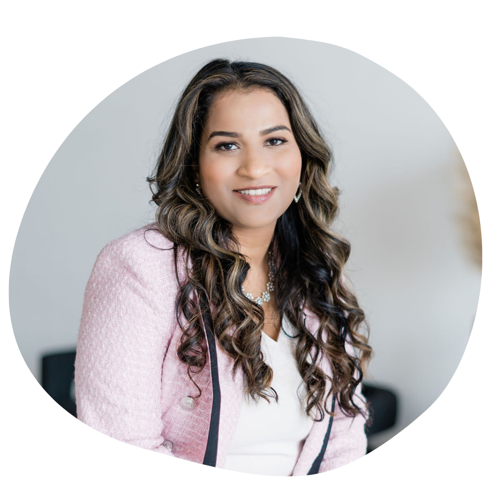 Beautiful Indian woman with long curly hair wears a pink blazer and smiles gently at the camera