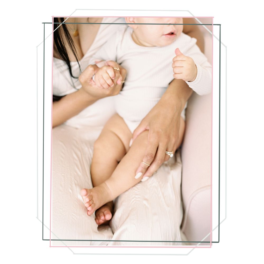 Rectangular photo of a baby in mom's lap, zoomed in to show mom's bands and baby's legs. Faces aren't visible.