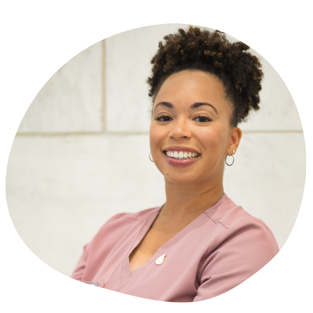 A woman with vibrant brown skin and pink scrubs smiles for a headshot